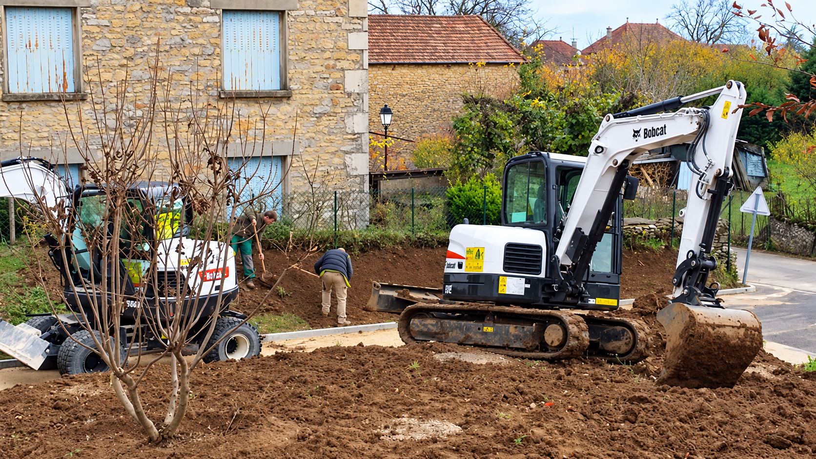 Une mini-pelle Bobcat blanche travaille la terre sur un chantier pendant que deux ouvriers bêchent près d'une maison en pierre et d'une seconde machine.